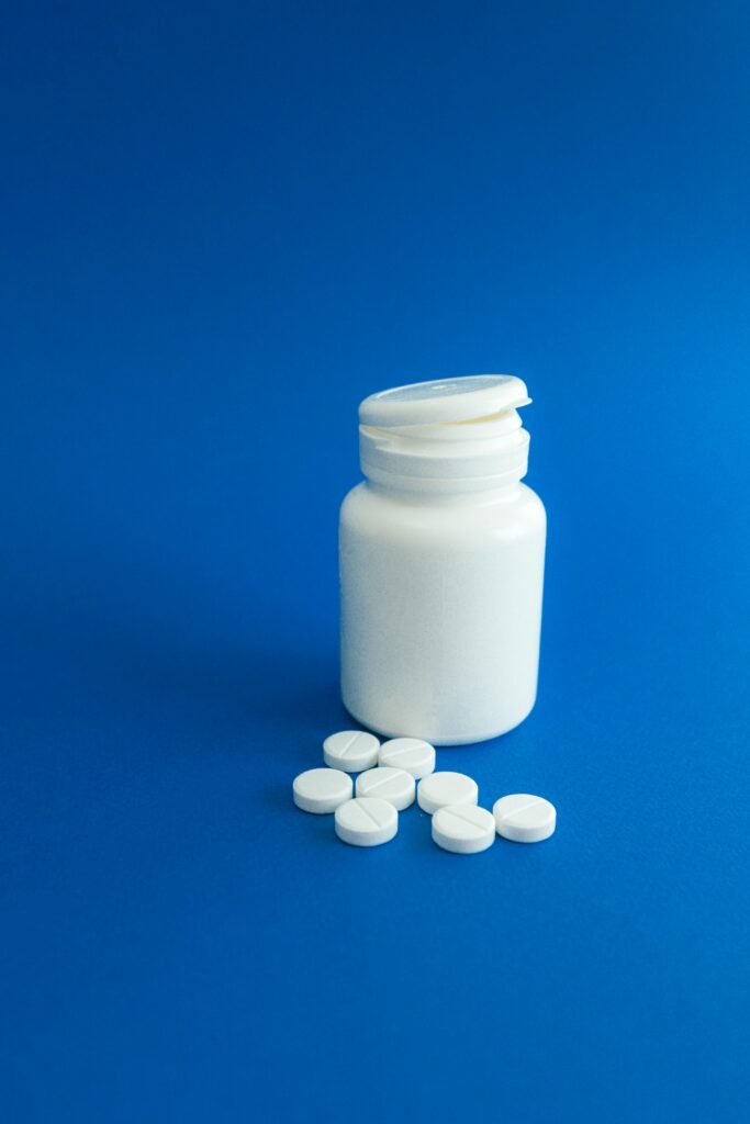 White pill bottle with scattered tablets on blue surface, ideal for healthcare themes.